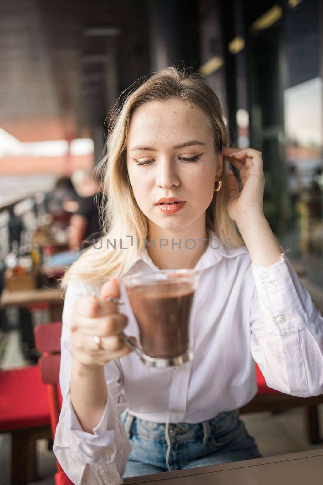 Gen z blonde woman drinks hot chocolate in summer cafe. Tasty beverage and break