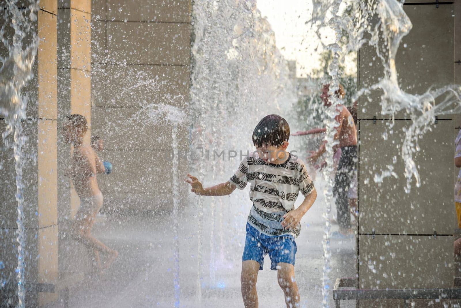 Boy having fun in water fountains. Child playing with a city fountain on hot summer day. Happy kids having fun in fountain. Summer weather. Active leisure, lifestyle and vacation.