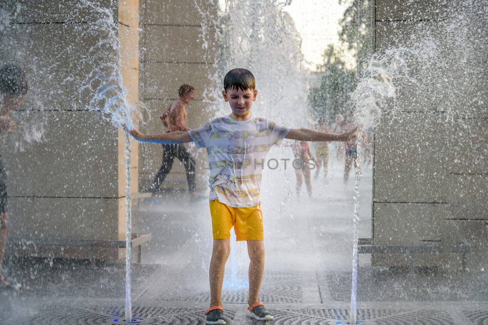 Boy having fun in water fountains. Child playing with a city fountain on hot summer day. Happy kids having fun in fountain. Summer weather. Active leisure, lifestyle and vacation by Kobysh