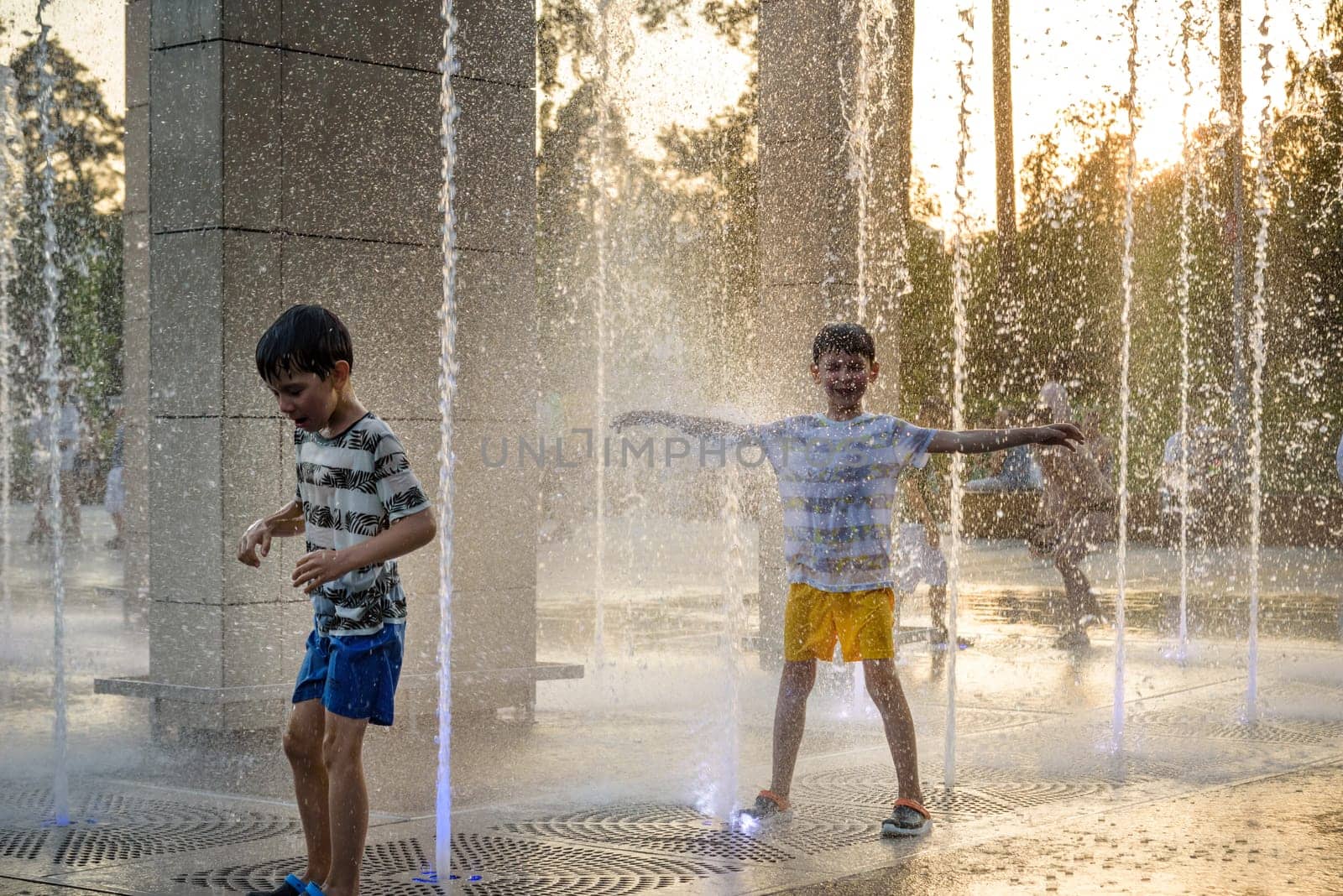 Boys jumping in water fountains. Children playing with a city fountain on hot summer day. Happy friends having fun in fountain. Summer weather. Friendship, lifestyle and vacation.