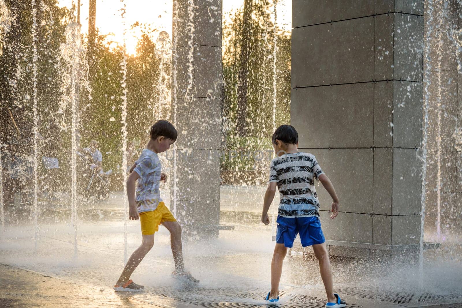 Boys jumping in water fountains. Children playing with a city fo by Kobysh