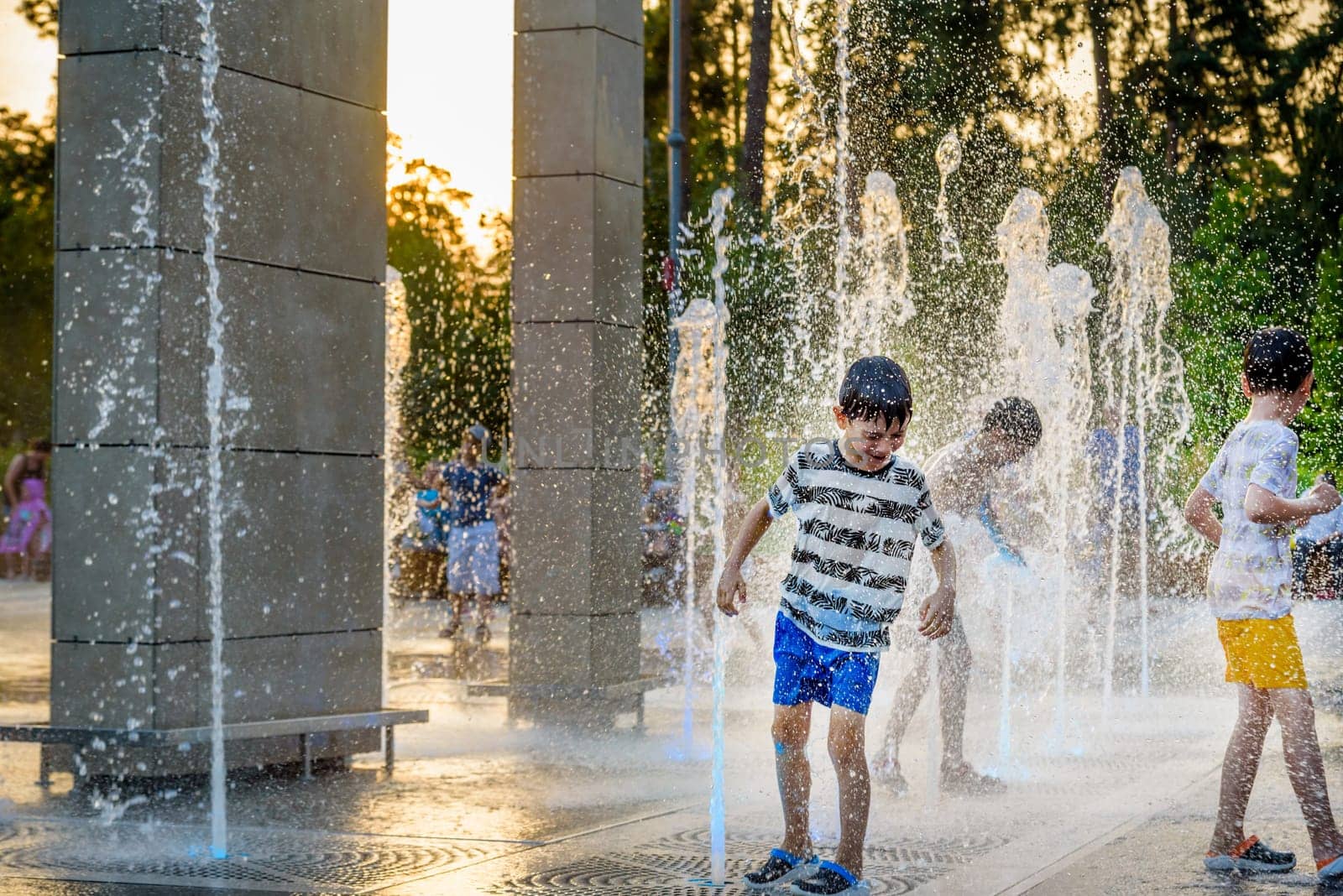 Boys jumping in water fountains. Children playing with a city fountain on hot summer day. Happy friends having fun in fountain. Summer weather. Friendship, lifestyle and vacation by Kobysh
