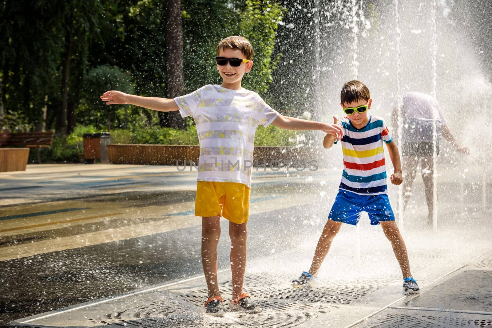 Boy having fun in water fountains. Child playing with a city fountain on hot summer day. Happy kids having fun in fountain. Summer weather. Active leisure, lifestyle and vacation by Kobysh