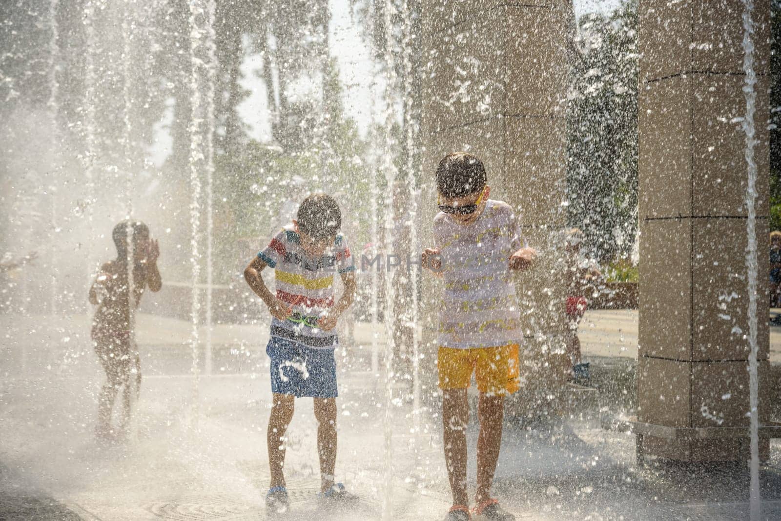 Boy having fun in water fountains. Child playing with a city fountain on hot summer day. Happy kids having fun in fountain. Summer weather. Active leisure, lifestyle and vacation.