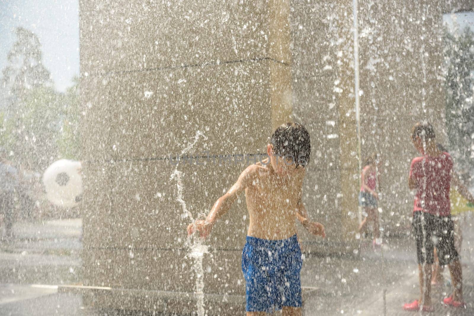 Boy having fun in water fountains. Child playing with a city fountain on hot summer day. Happy kids having fun in fountain. Summer weather. Active leisure, lifestyle and vacation.