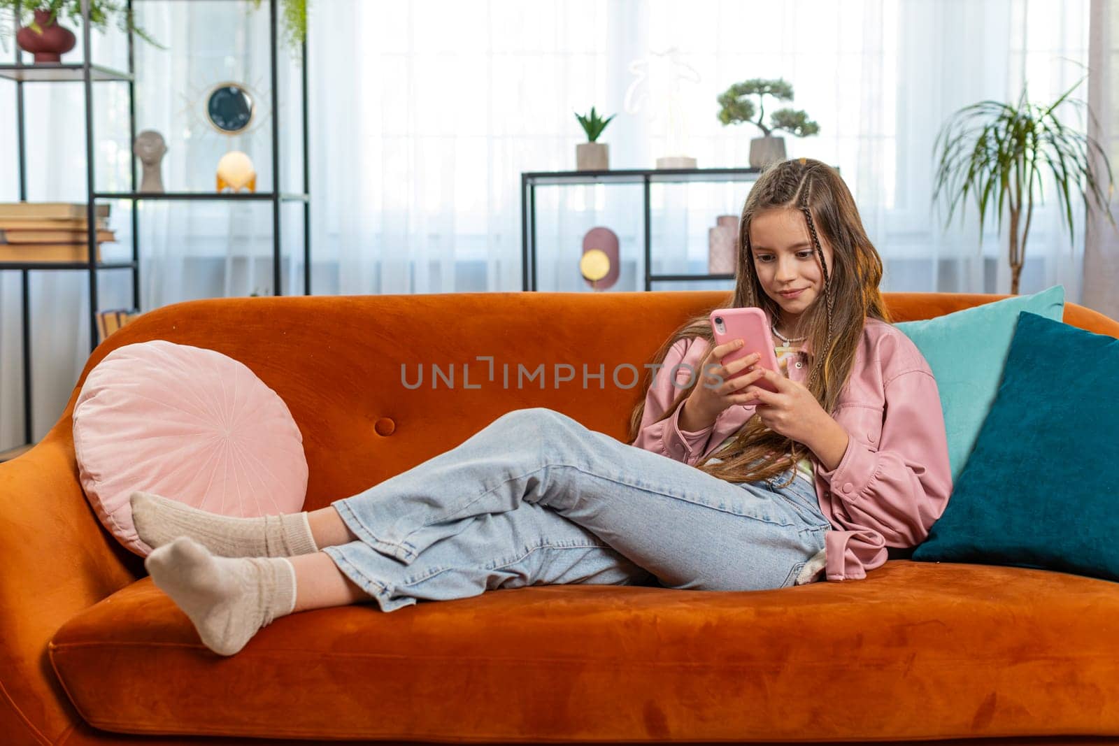 Young girl texting share messages content on smartphone social media applications online watching relax movie. Female Caucasian teenager kid child uses mobile phone sits on sofa in living room at home