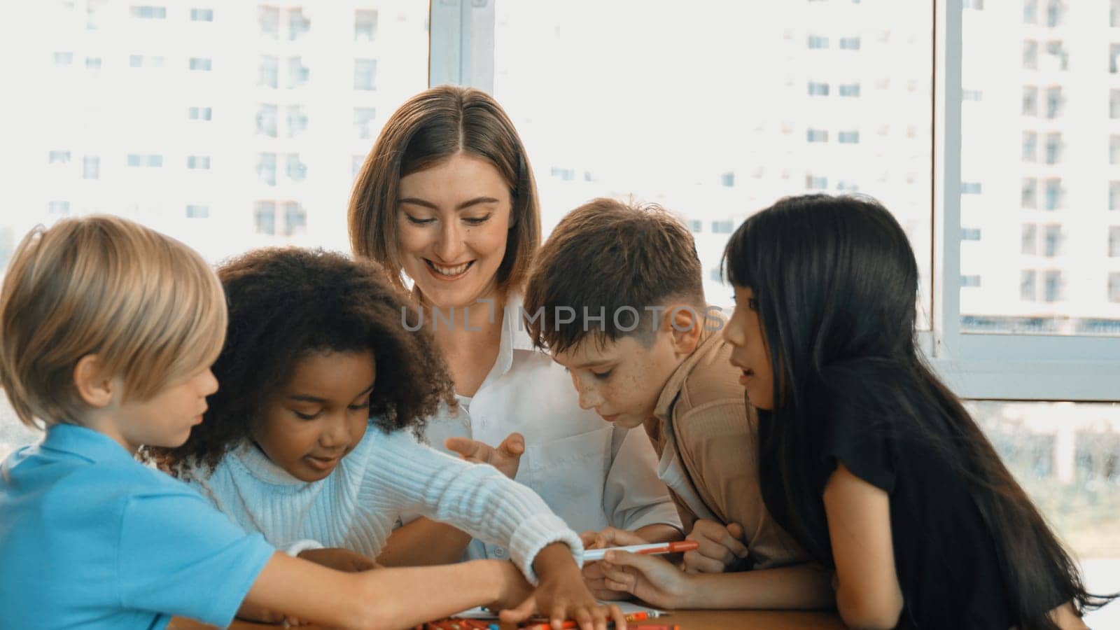 Professional caucasian teacher telling story to diverse student while sitting at table with storybook and colored book. Smart learner listening story while colored picture from instructor. Erudition.