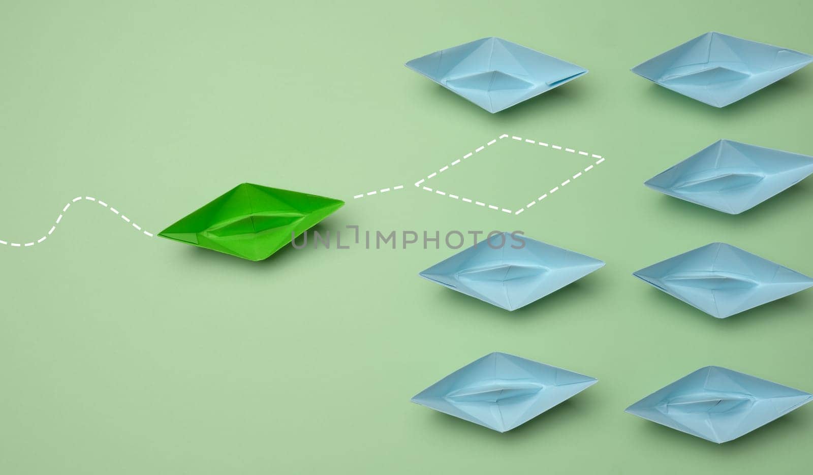 Group of blue paper boats heading in one direction and one green one heading in the opposite direction. The concept of individuality, uniqueness and talent of the employee. Get away from the influence