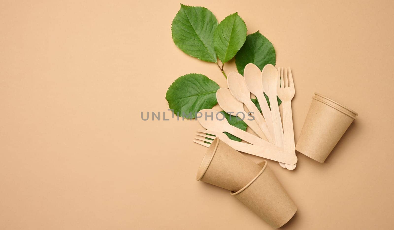 Paper cups, wooden spoons and forks on a beige background, top view