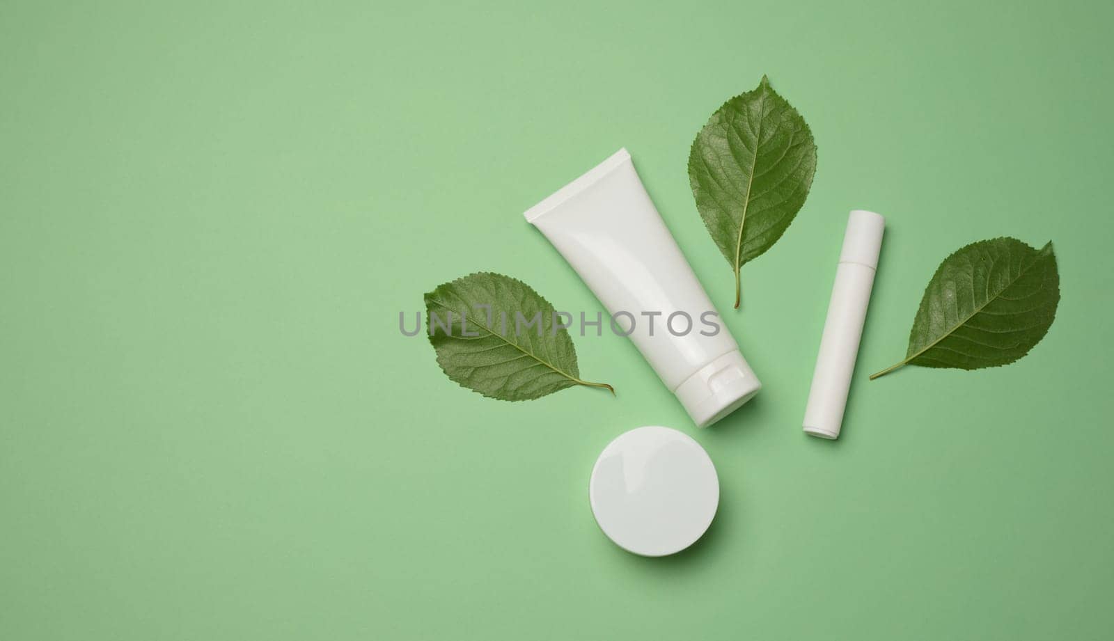 White plastic tubes, jars, and containers for cosmetic products on a green background by ndanko