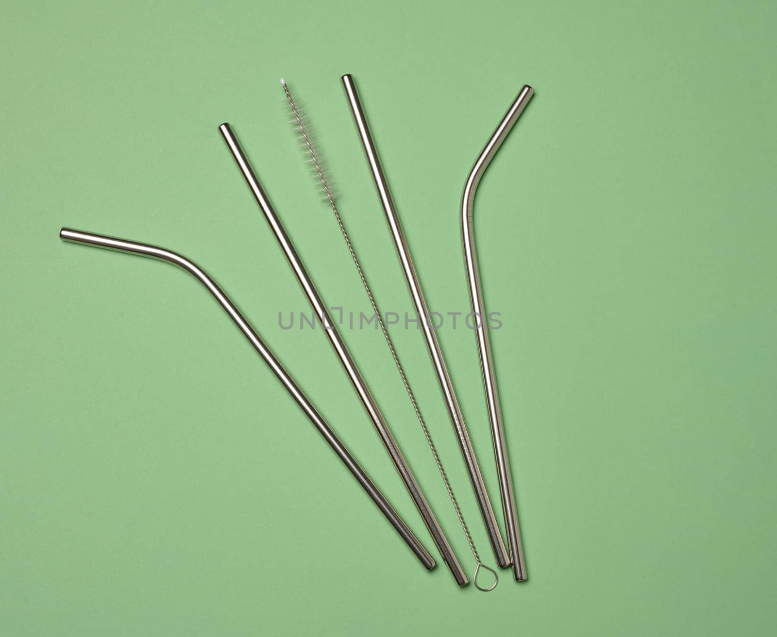 Metal straws for cocktails and a cleaning brush on a green background, top view