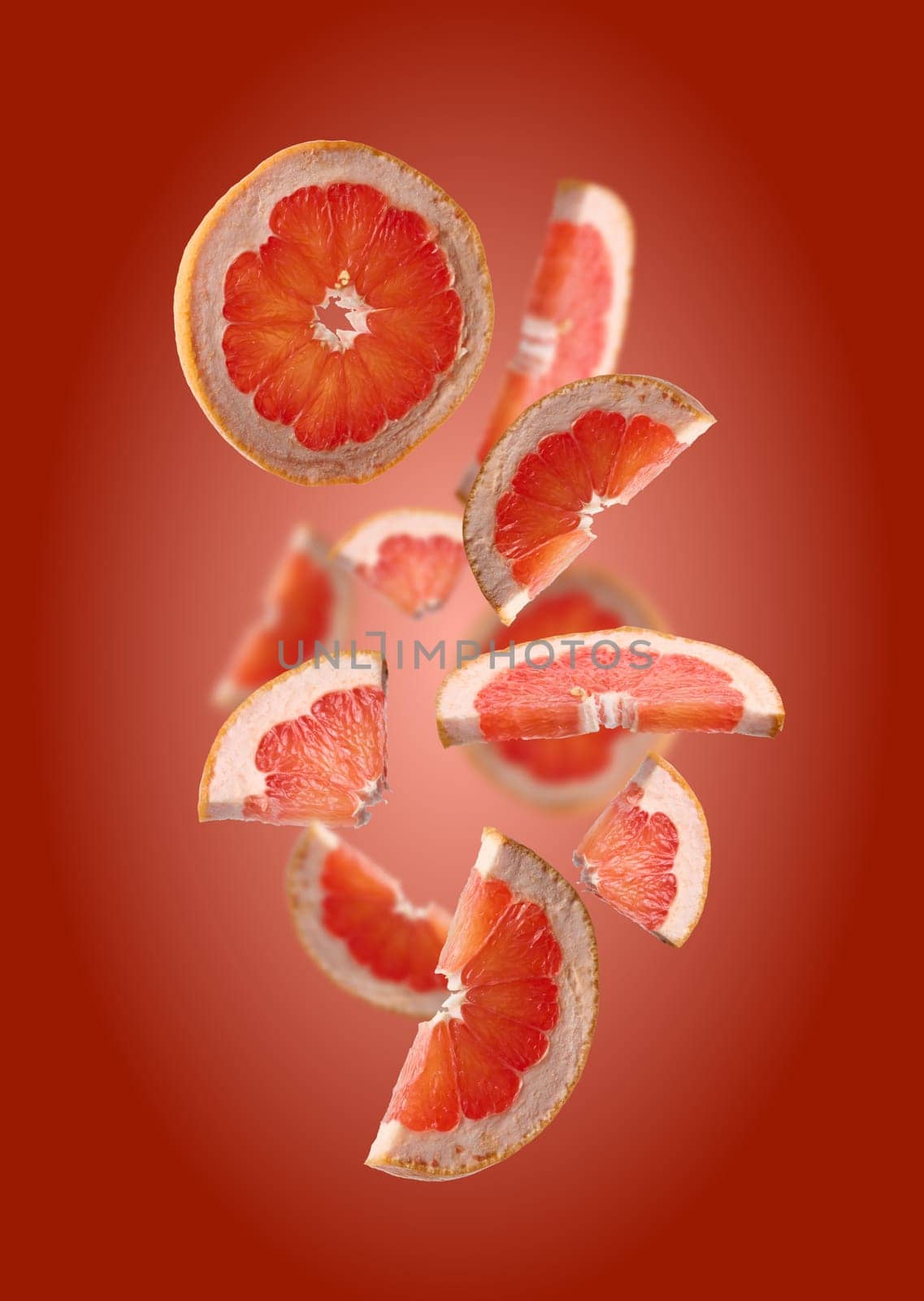 Various pieces of ripe grapefruit on a red background, fruit slices levitate