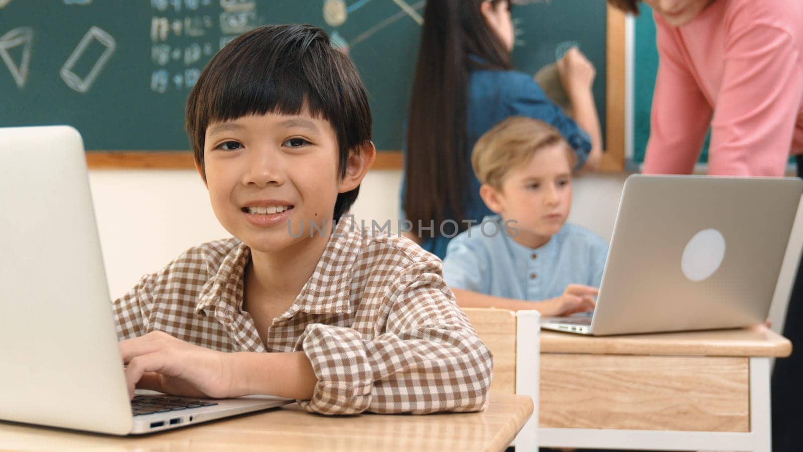 Cute boy coding engineering prompt while attractive girl drawing picture at blackboard. Caucasian boy asking teacher a question about programing software system to generate AI at STEM class. Pedagogy.