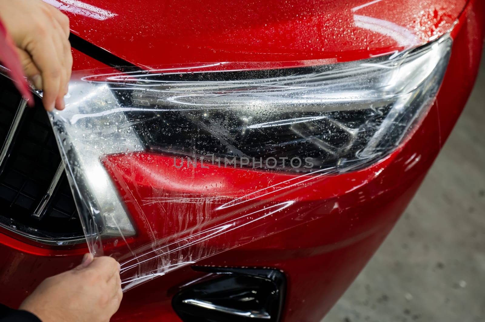 The master applies vinyl film to the headlight of a red car