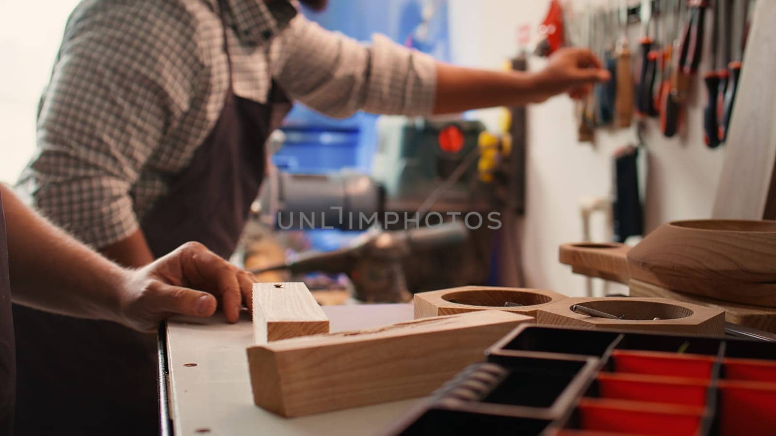 Woodworker using power drill to create holes for dowels in wooden board, close up. Carpenter sinks screws into wooden surfaces with electric tool, doing precise drilling for seamless joinery, camera B