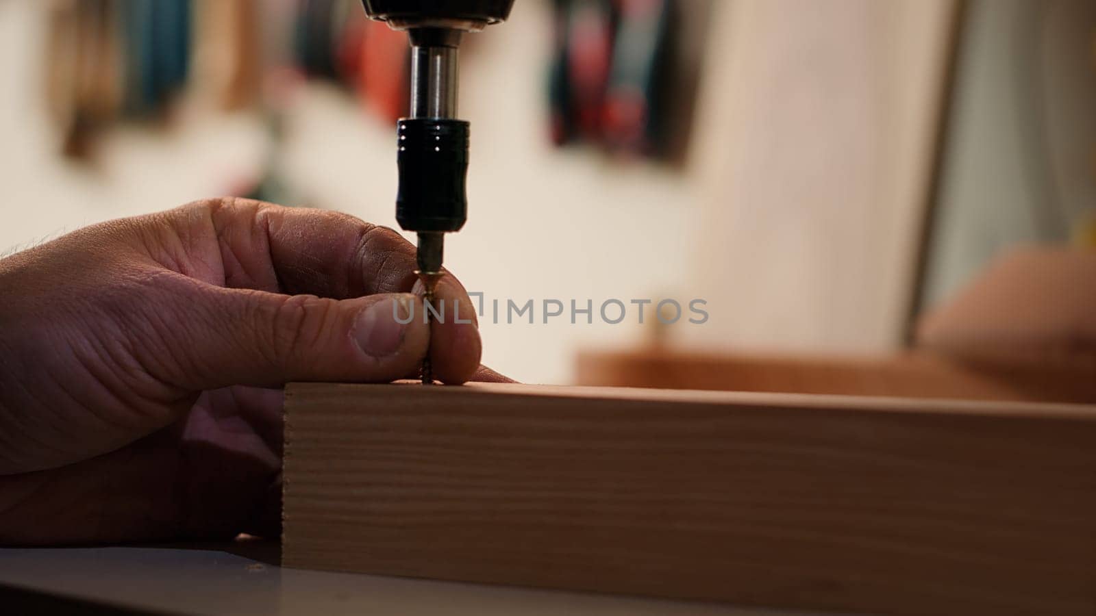 Carpenter sinks screws into wooden surfaces with power drill, close up by DCStudio