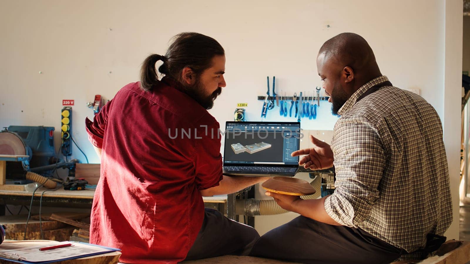 African american manufacturer and colleague comparing wood art piece with schematic displayed on CAD software on laptop. Woodworking professionals crosschecking wooden object with blueprint, camera B