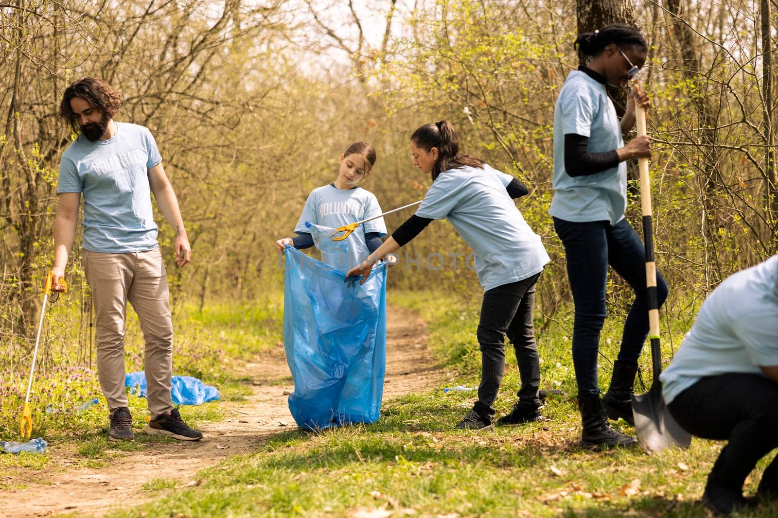 Group of diverse activists collecting trash from the forest and recycling in a garbage disposal bag, cleanup responsibility. Ecology volunteers picking up junk and plastic waste.