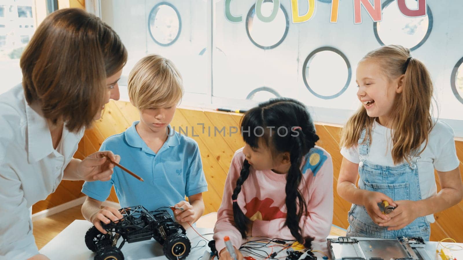 Young smart caucasian teacher teaching diverse students about electronic board. Multicultural children learn about digital electrical tool and fixing motherboard by using chips and wires. Erudition.