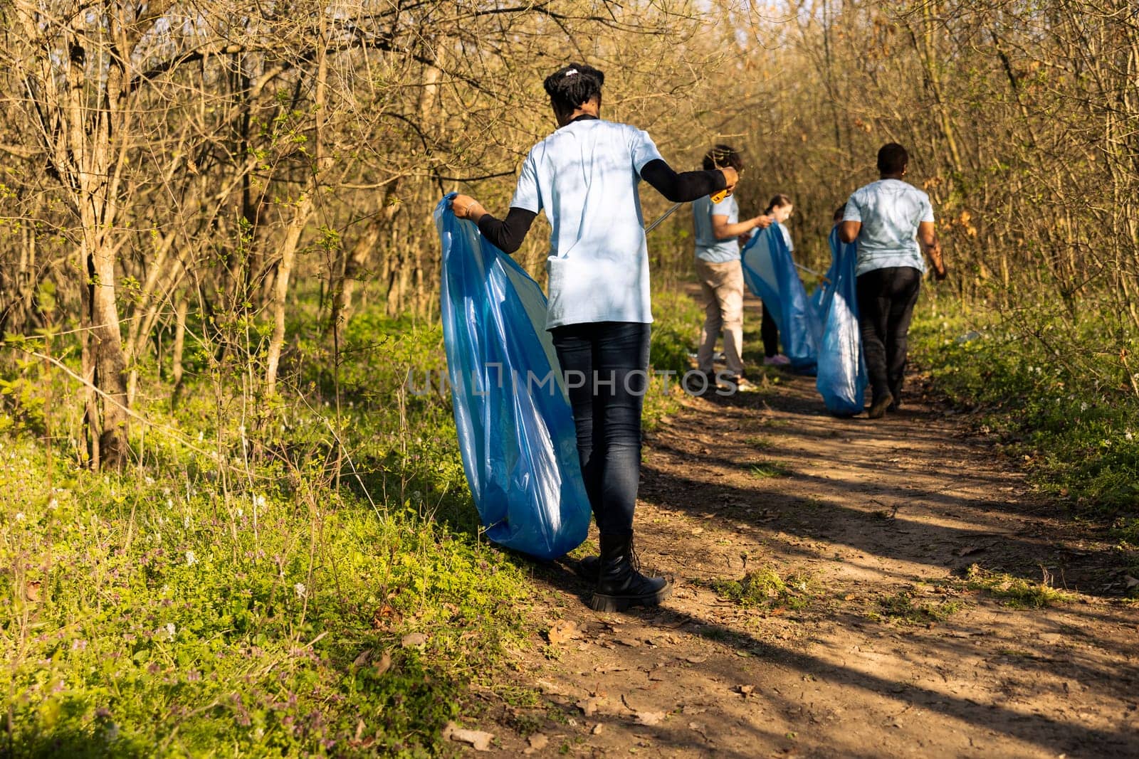 African american climate change volunteer grabbing trash in a bag, working to protect the natural environment. Volunteering for nature conservation and community service action.