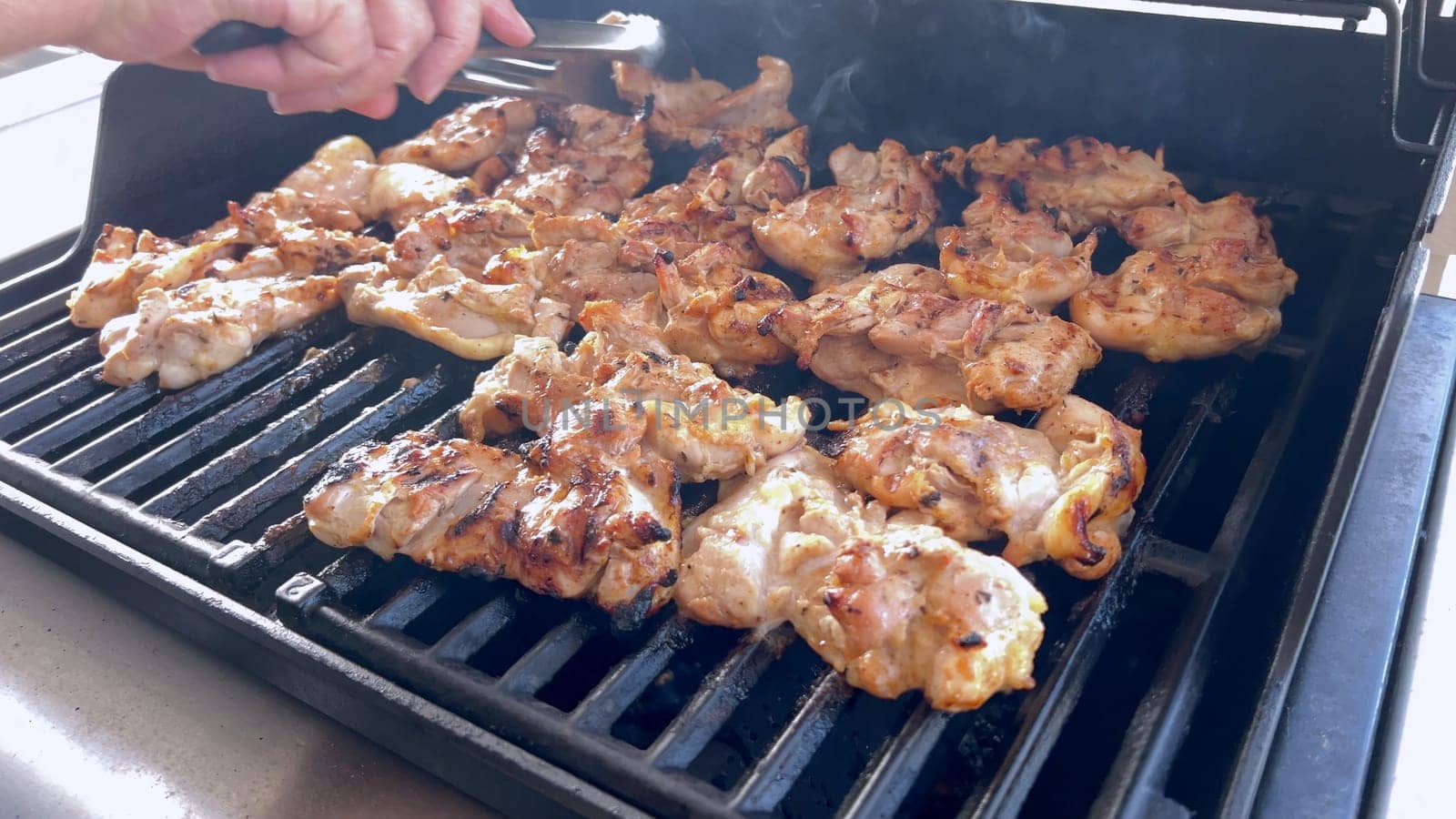 A close-up image capturing the process of grilling marinated chicken pieces, with a person expertly flipping them to ensure even cooking on a classic outdoor barbecue grill.