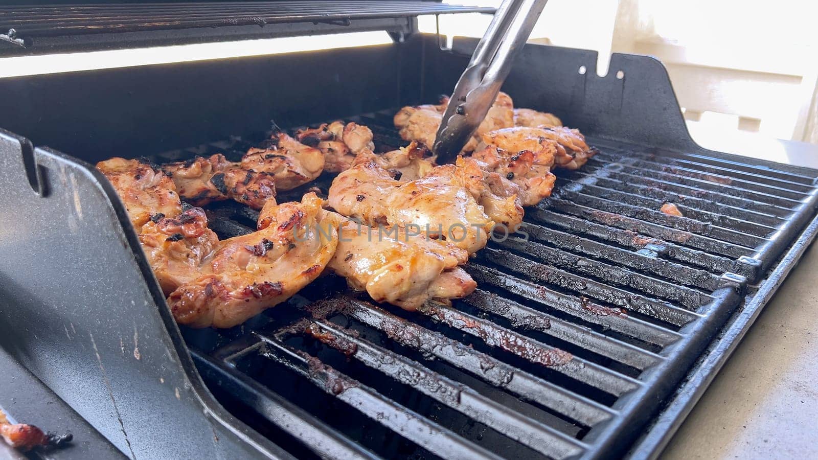 A close-up image capturing the process of grilling marinated chicken pieces, with a person expertly flipping them to ensure even cooking on a classic outdoor barbecue grill.
