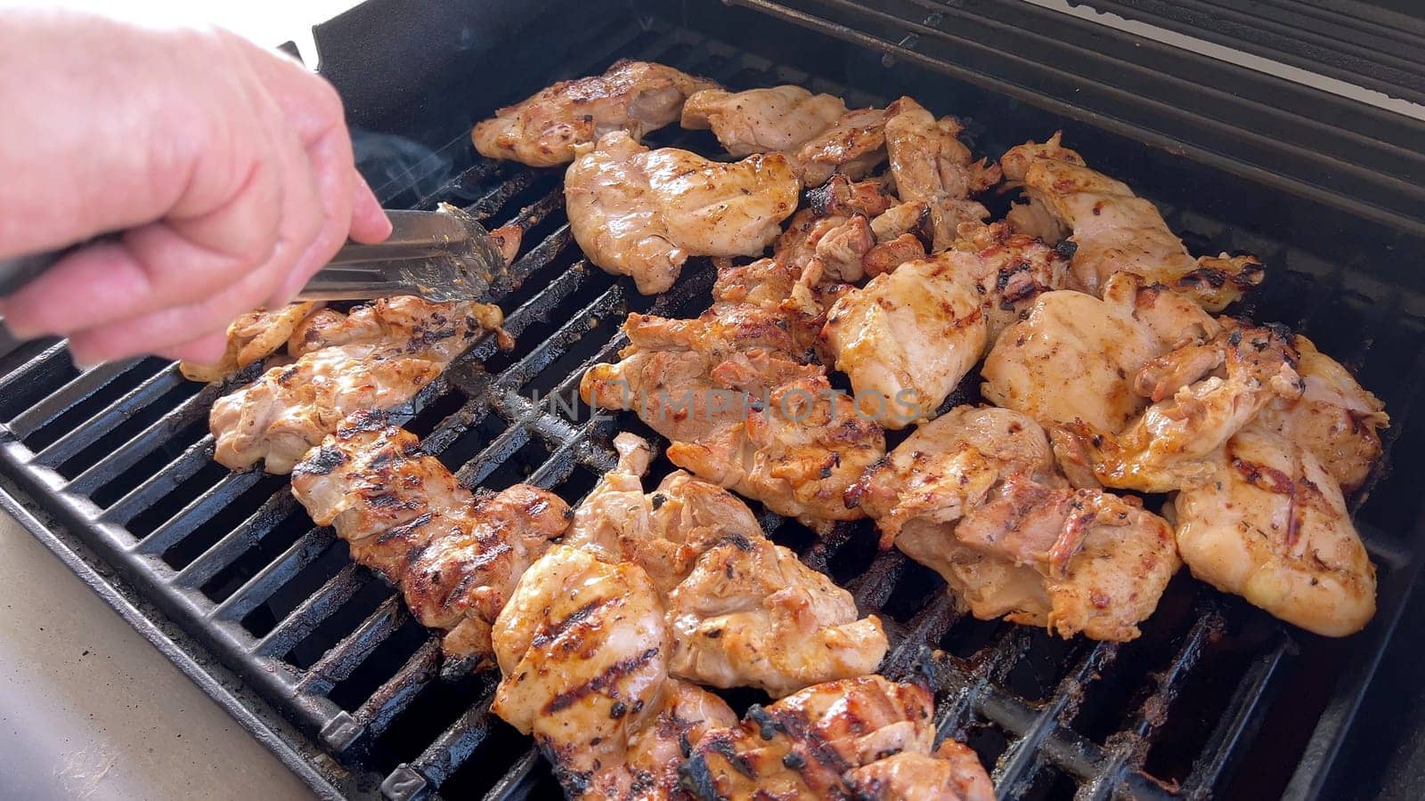 A close-up image capturing the process of grilling marinated chicken pieces, with a person expertly flipping them to ensure even cooking on a classic outdoor barbecue grill.