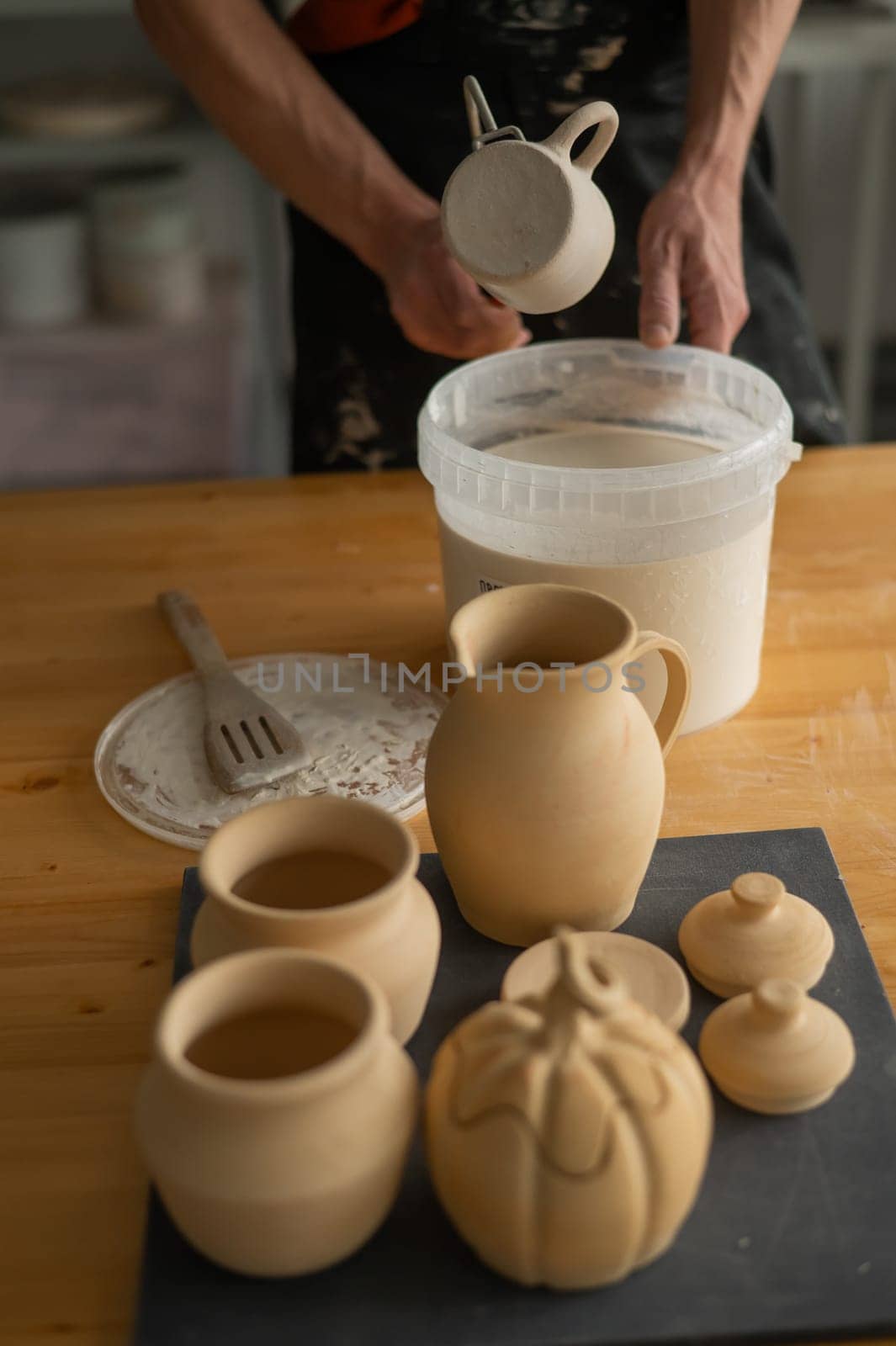 Close-up of a potter's hands glazing a ceramic mug. Vertical photo