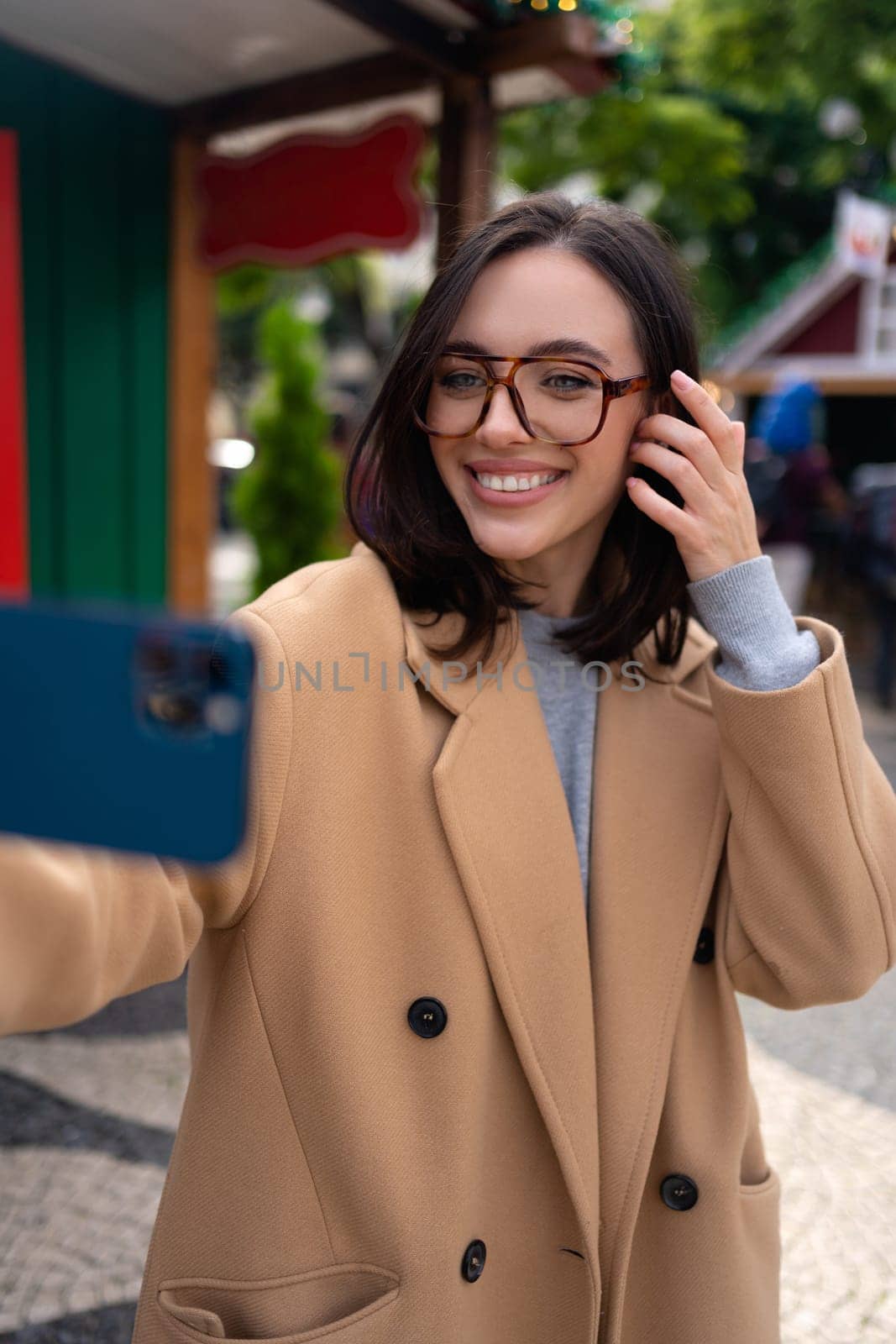 Beautiful woman using mobile phone for video call outdoors. Smiling girl looking smart phone screen in a city street. Happy smiling woman chatting on smartphone warm autumn day. Vertical photo
