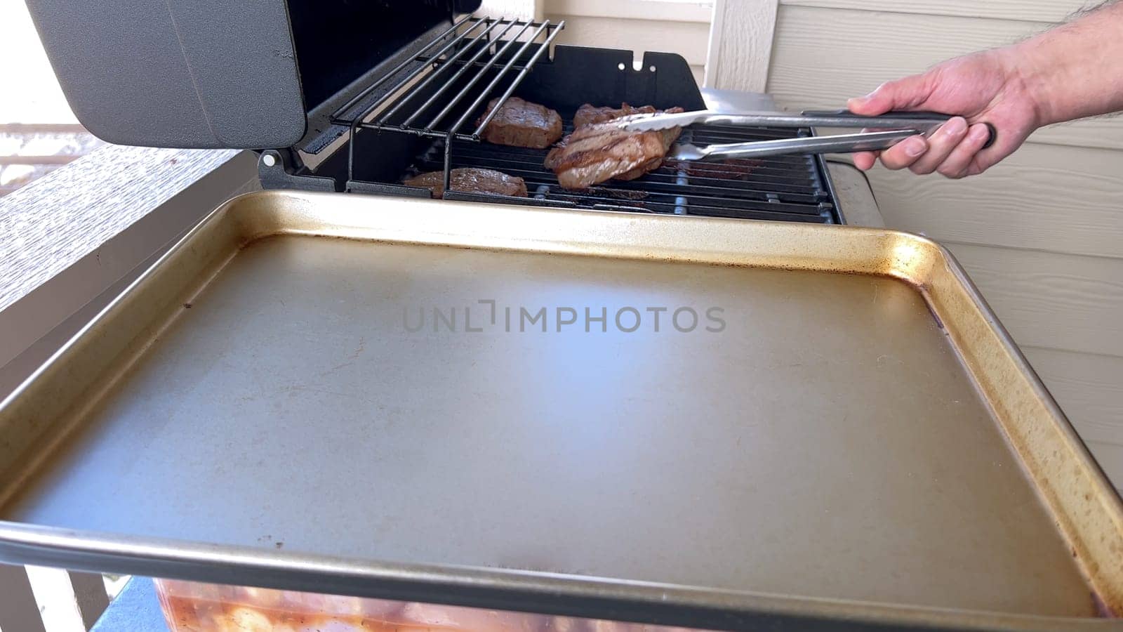 Several thick steaks with grill marks cooking to perfection on an outdoor grill, capturing the essence of a sunny barbecue day.