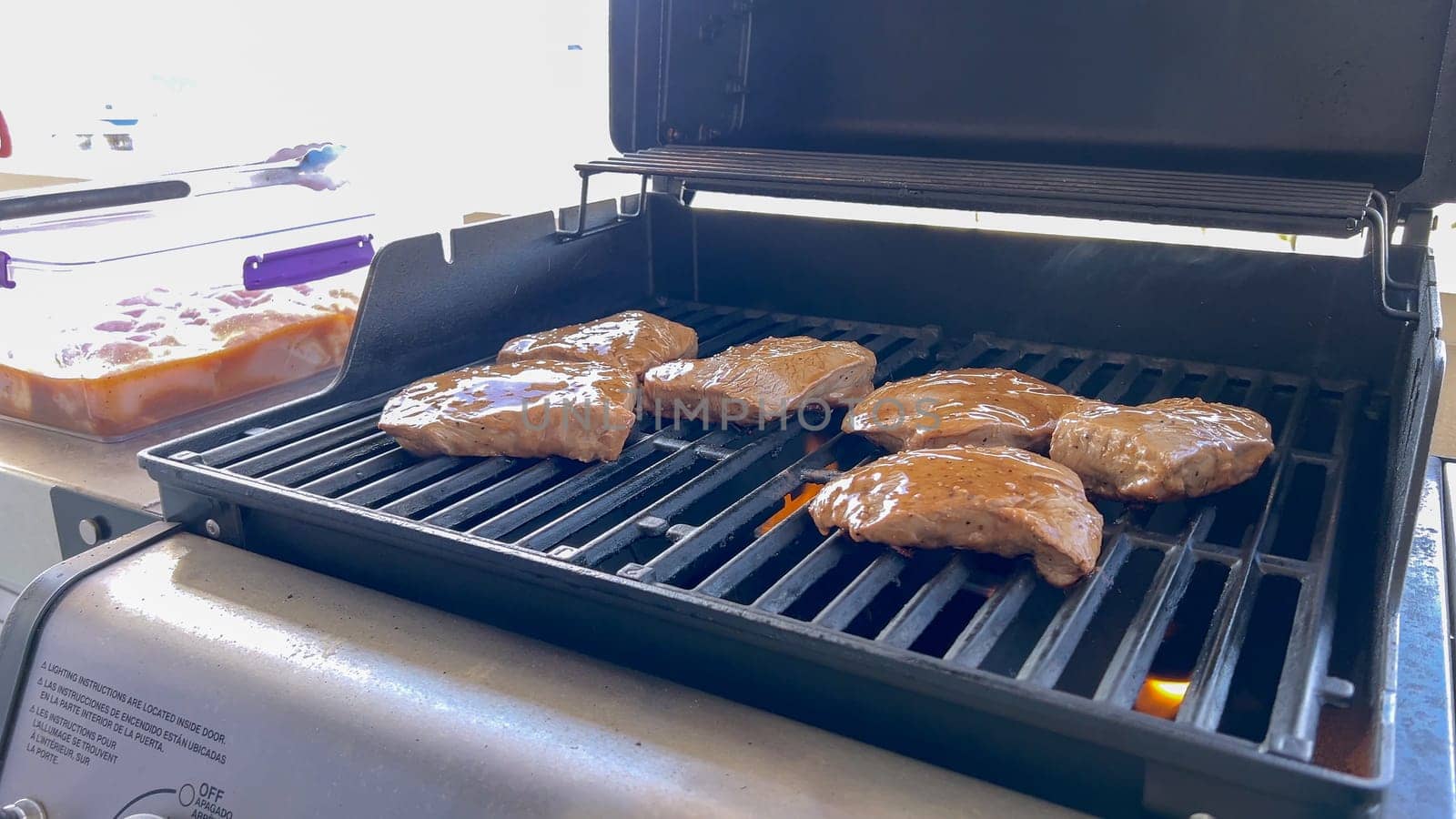 Several thick steaks with grill marks cooking to perfection on an outdoor grill, capturing the essence of a sunny barbecue day.