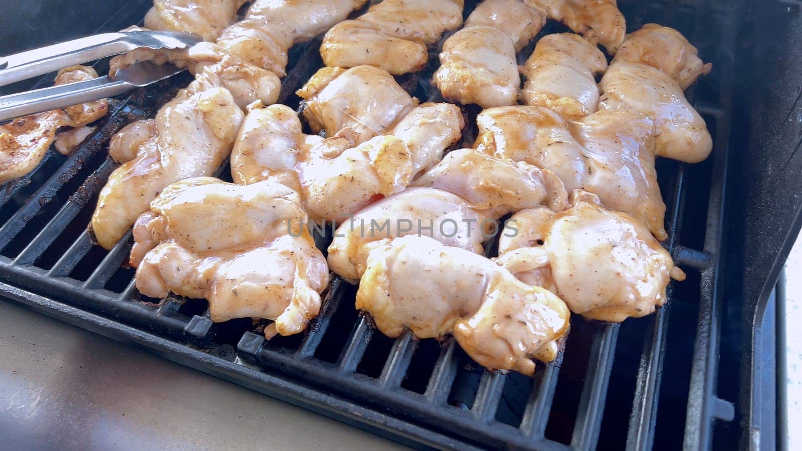 A close-up image capturing the process of grilling marinated chicken pieces, with a person expertly flipping them to ensure even cooking on a classic outdoor barbecue grill.