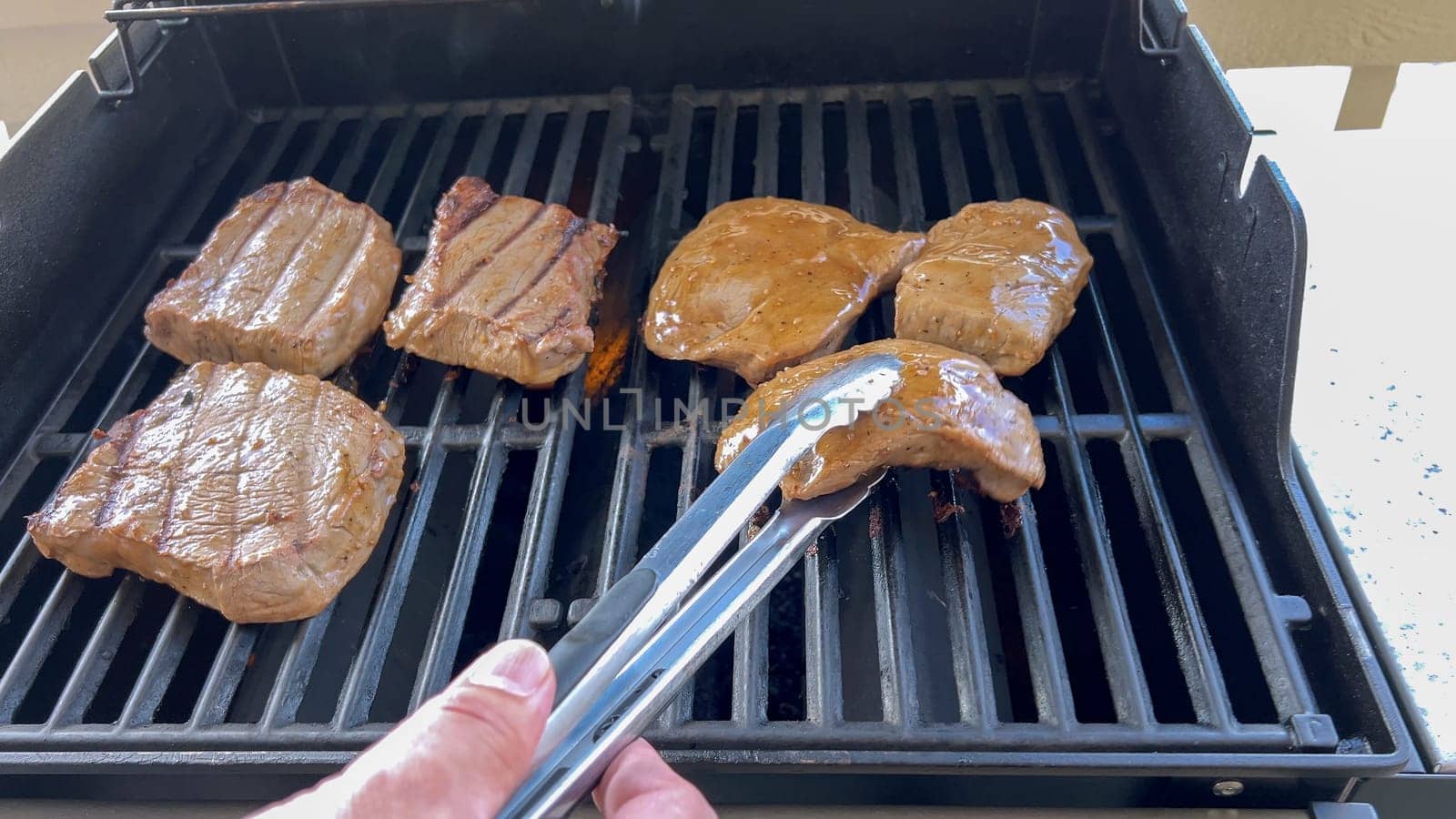 Several thick steaks with grill marks cooking to perfection on an outdoor grill, capturing the essence of a sunny barbecue day.