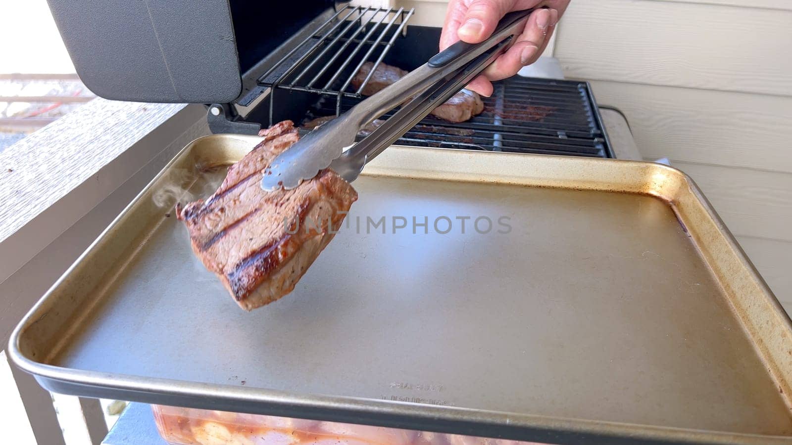 Several thick steaks with grill marks cooking to perfection on an outdoor grill, capturing the essence of a sunny barbecue day.