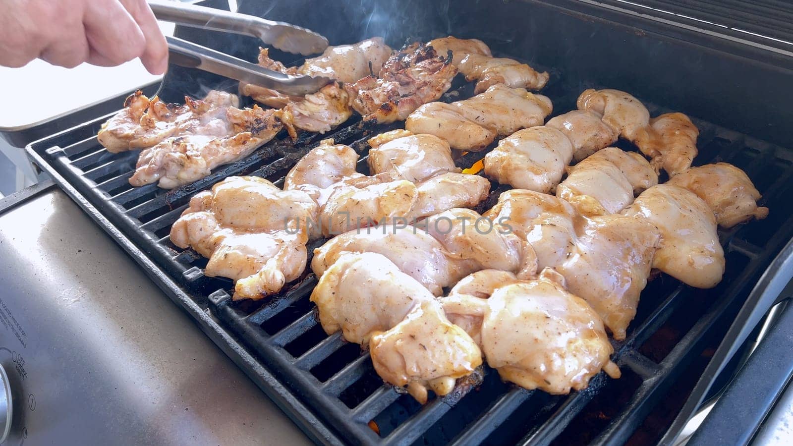 A close-up image capturing the process of grilling marinated chicken pieces, with a person expertly flipping them to ensure even cooking on a classic outdoor barbecue grill.