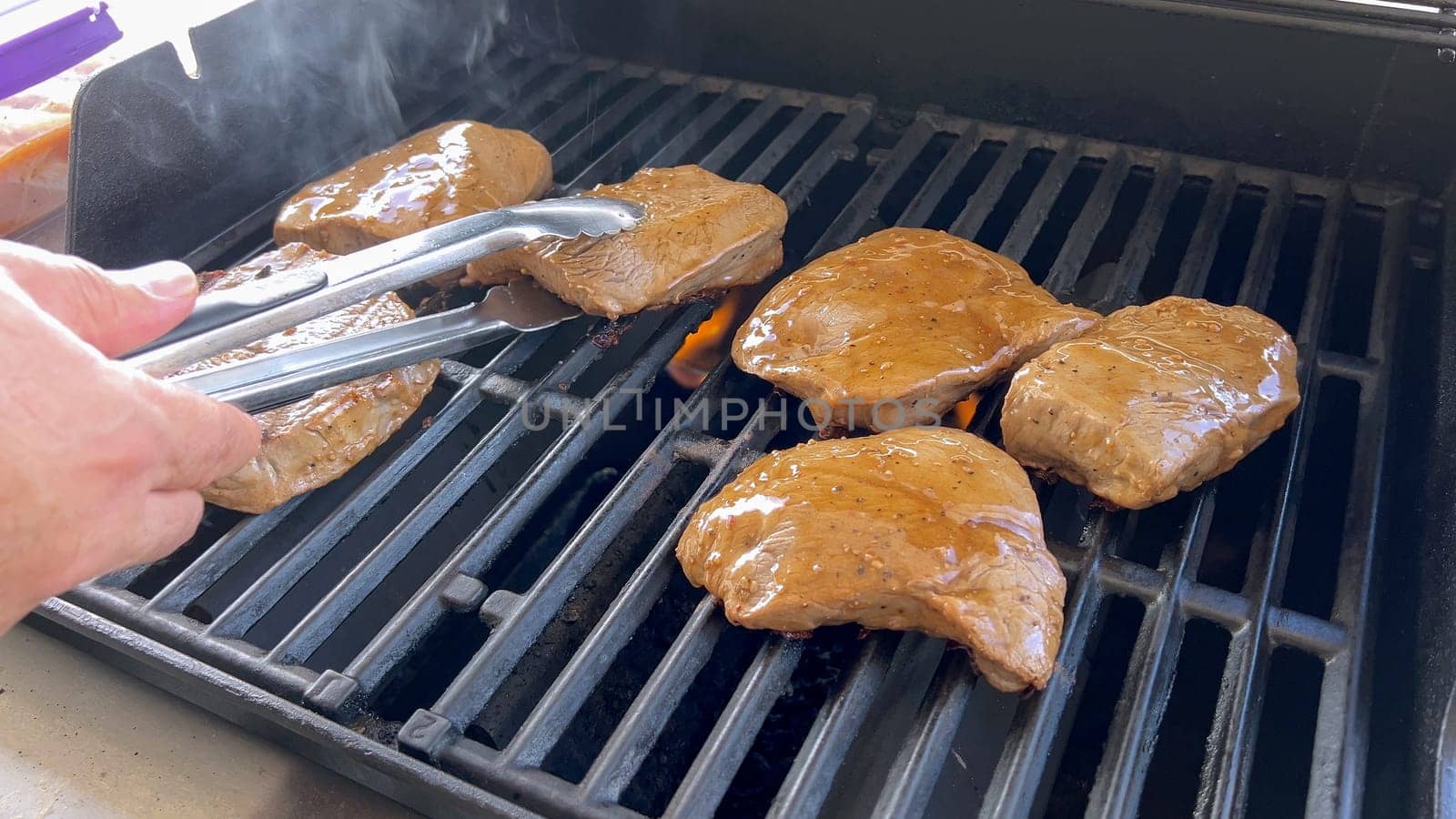 Several thick steaks with grill marks cooking to perfection on an outdoor grill, capturing the essence of a sunny barbecue day.