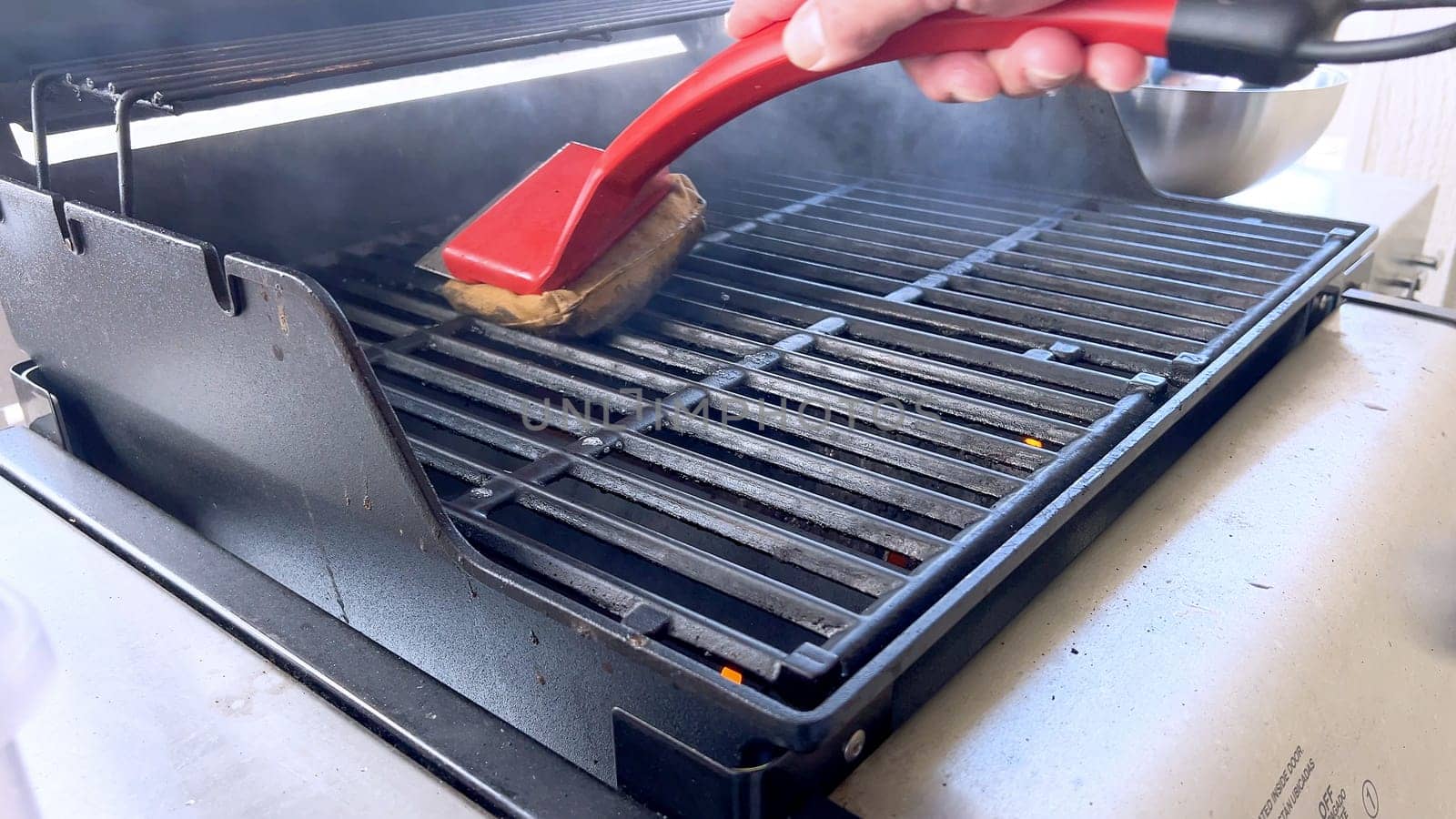 Cleaning a Barbecue Grill with a Brush After Cooking by arinahabich