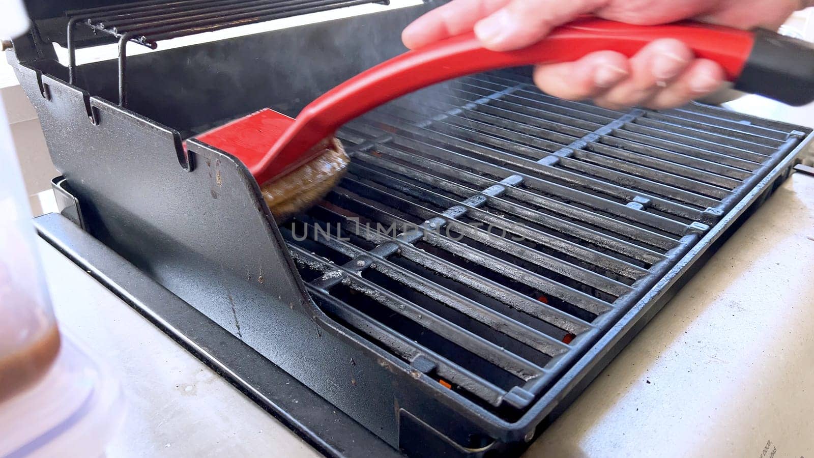 Cleaning a Barbecue Grill with a Brush After Cooking by arinahabich