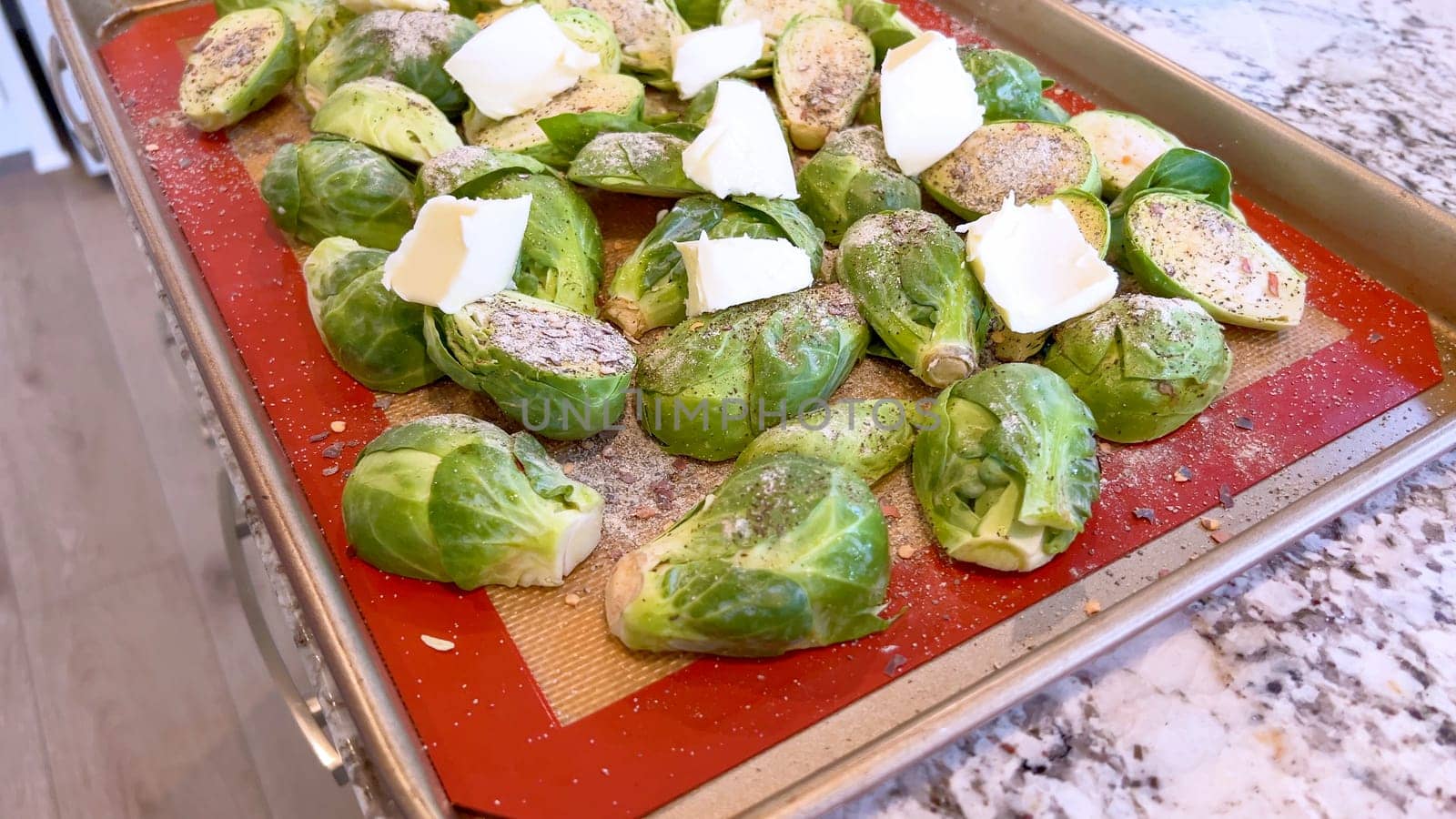 Fresh Brussels sprouts seasoned with spices and topped with slices of butter, arranged on a baking sheet, ready to be roasted to perfection.