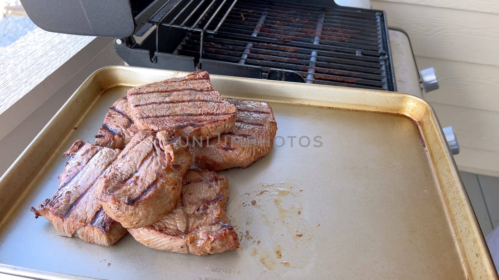 Several thick steaks with grill marks cooking to perfection on an outdoor grill, capturing the essence of a sunny barbecue day.