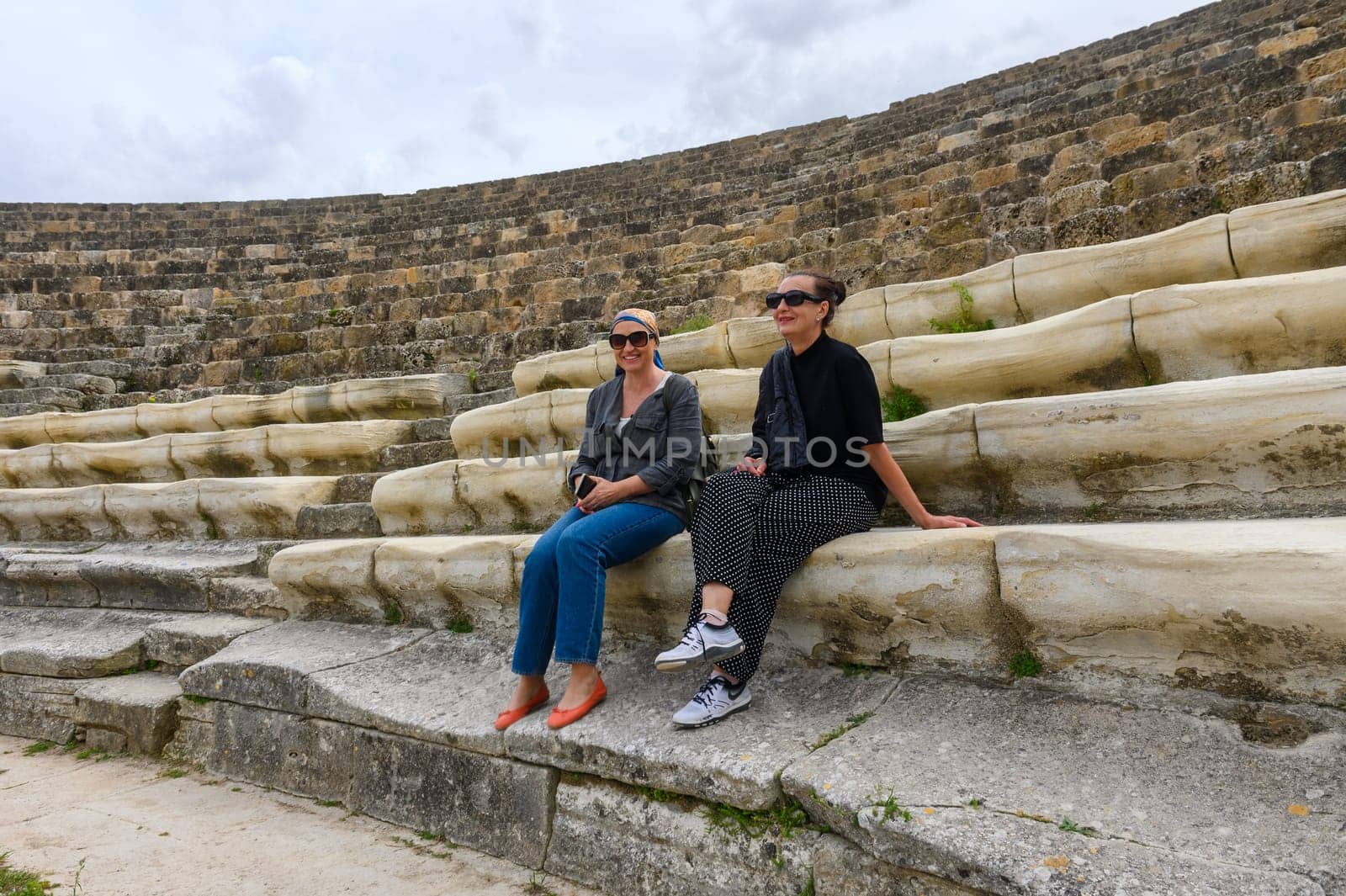 2 women sitting in an amphitheater in an ancient ruined city, reconstruction, restoration 1