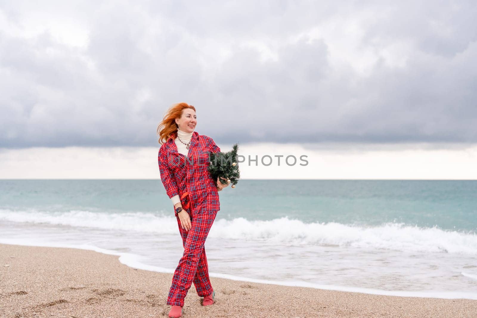 Sea Lady in plaid shirt with a christmas tree in her hands enjoys beach. Coastal area. Christmas, New Year holidays concep by Matiunina