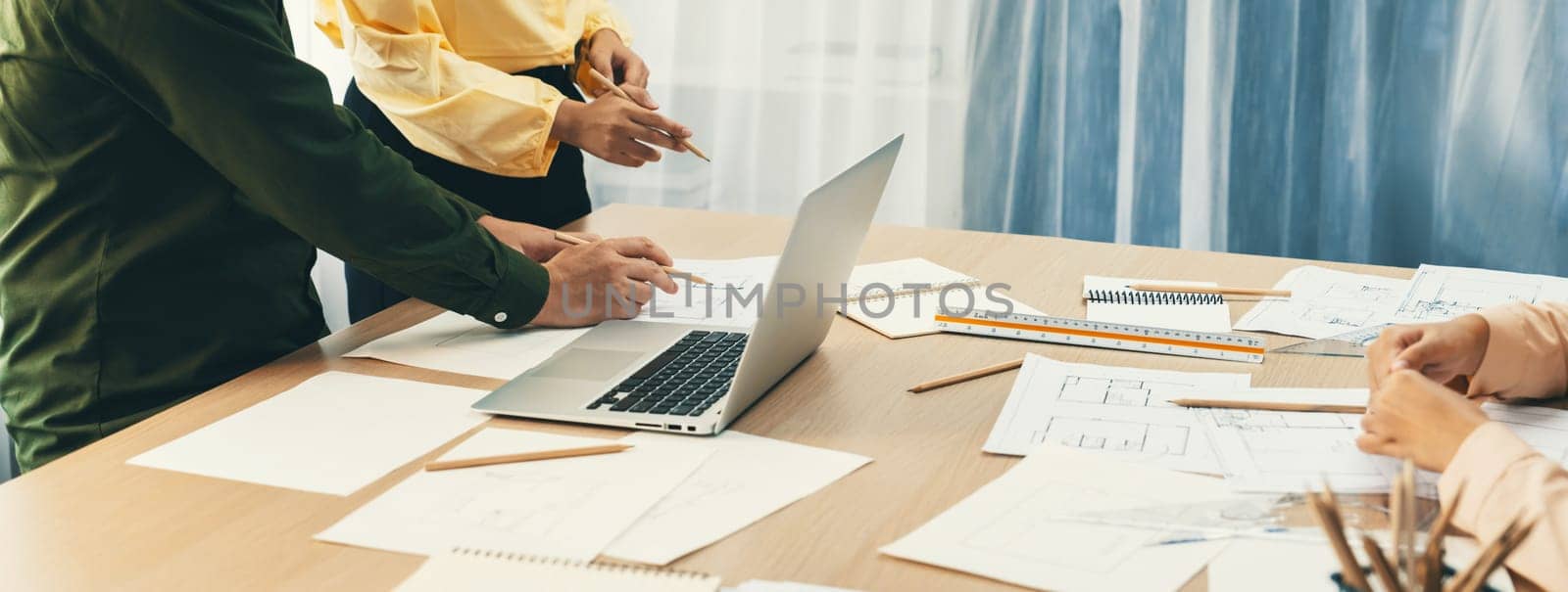 Professional architect edited blueprint by using laptop while project manager point the mistake point at meeting room on meeting table with architectural document scatter around. Closeup. Delineation.