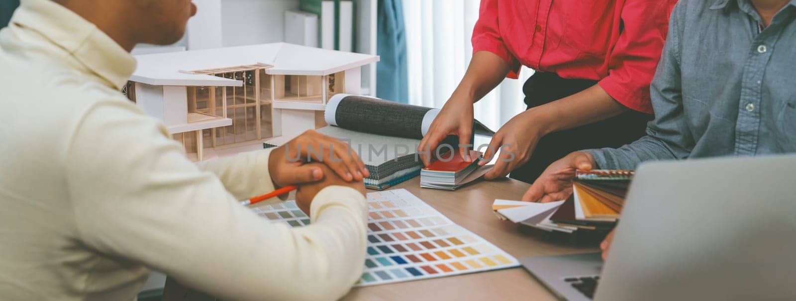 Skilled interior design team carefully selecting curtain materials while coworker selecting the color of curtain with house model placed on meeting table. Creative design concept. Variegated.