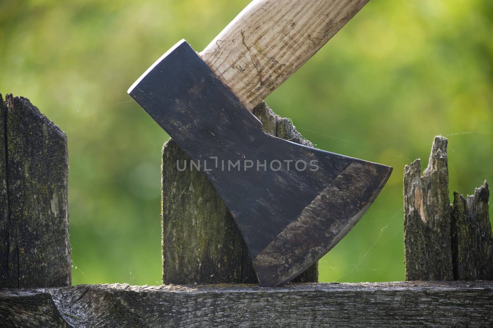 Close up of an axe with brown handle and dark grey blade embedded in an aged, cracked wooden fence post