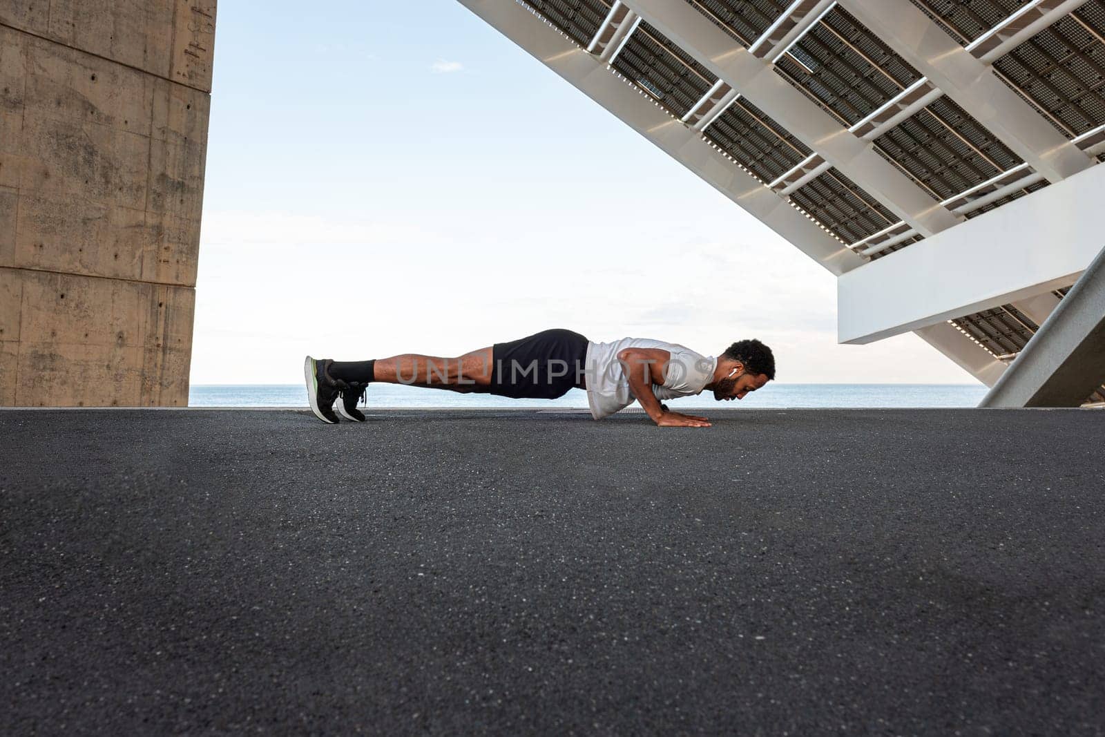 Side view of young African American male wearing sportswear doing push ups outdoors by Hoverstock