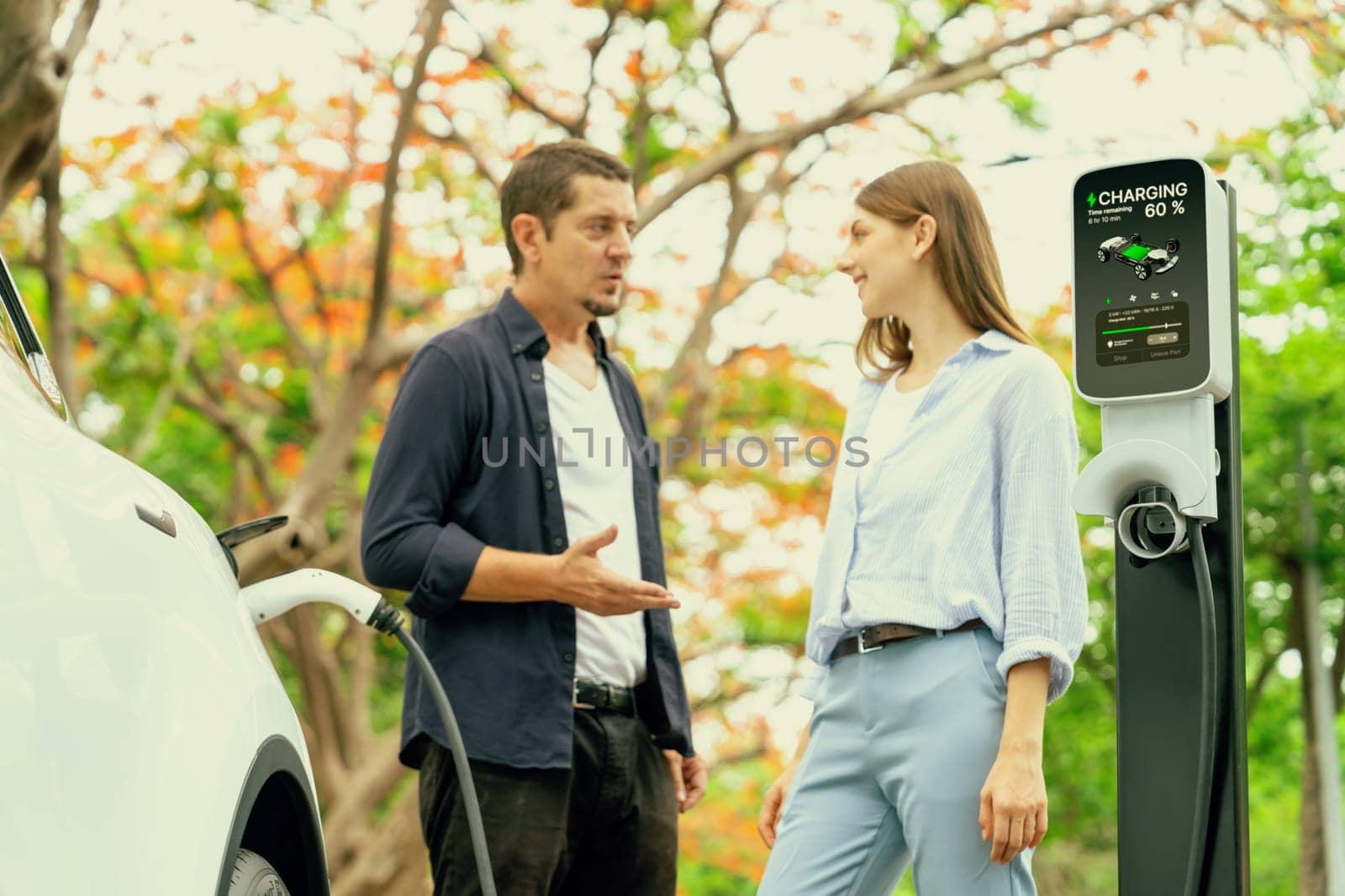 Lovely young couple recharging battery for electric car during autumnal road trip travel EV car in autumnal forest. Eco friendly travel on vacation during autumn. Exalt