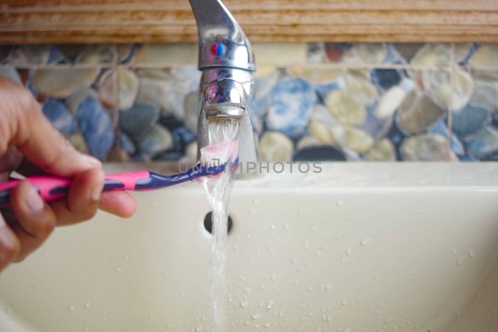 slow motion of holding toothbrush under flowing water in bathroom, closeup. by towfiq007