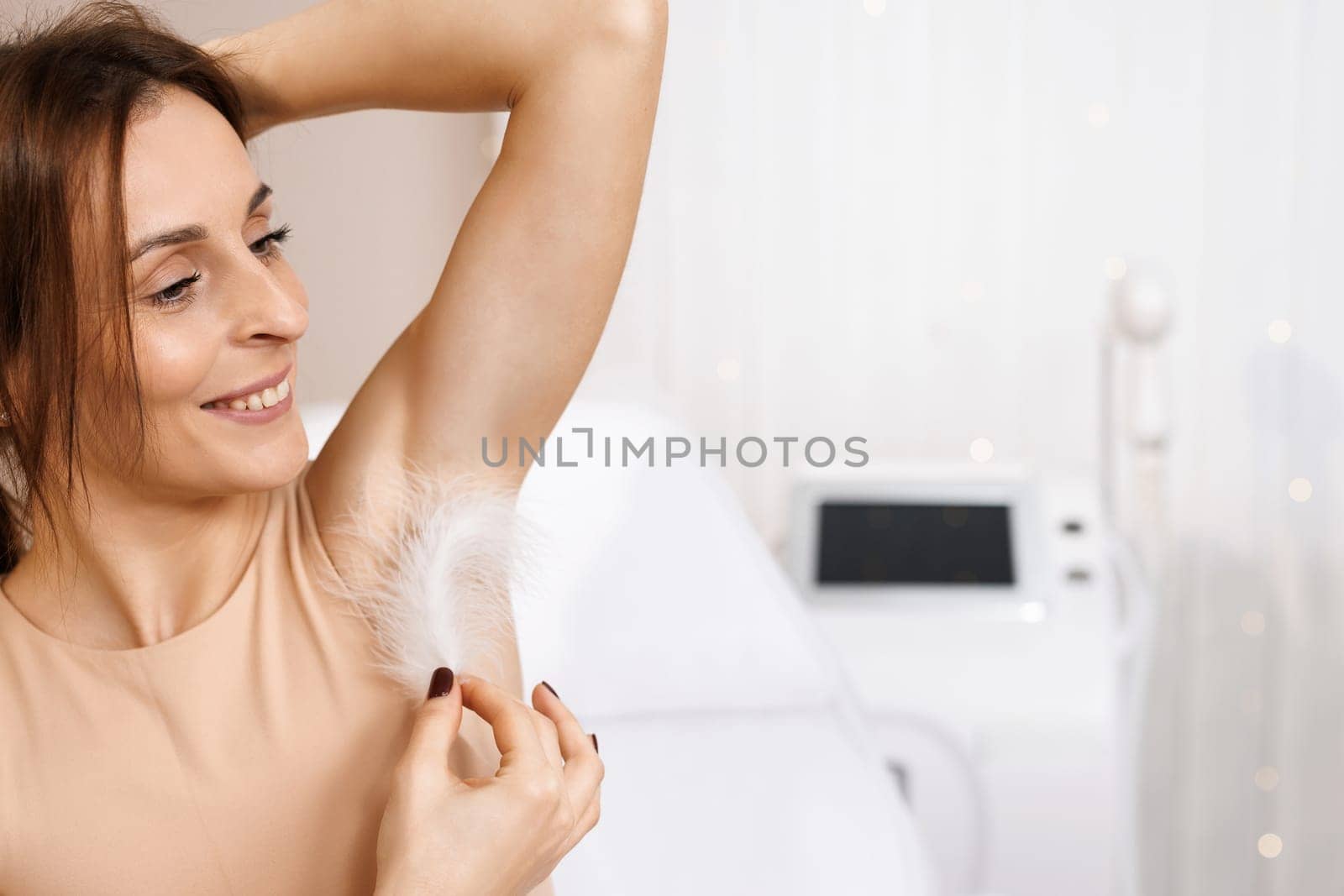 Armpit epilation, hair removal. Young woman holding her hands up and showing clean armpits, depilating smooth transparent skin. Portrait of beauty. Armpit care. Large white feather near the skin