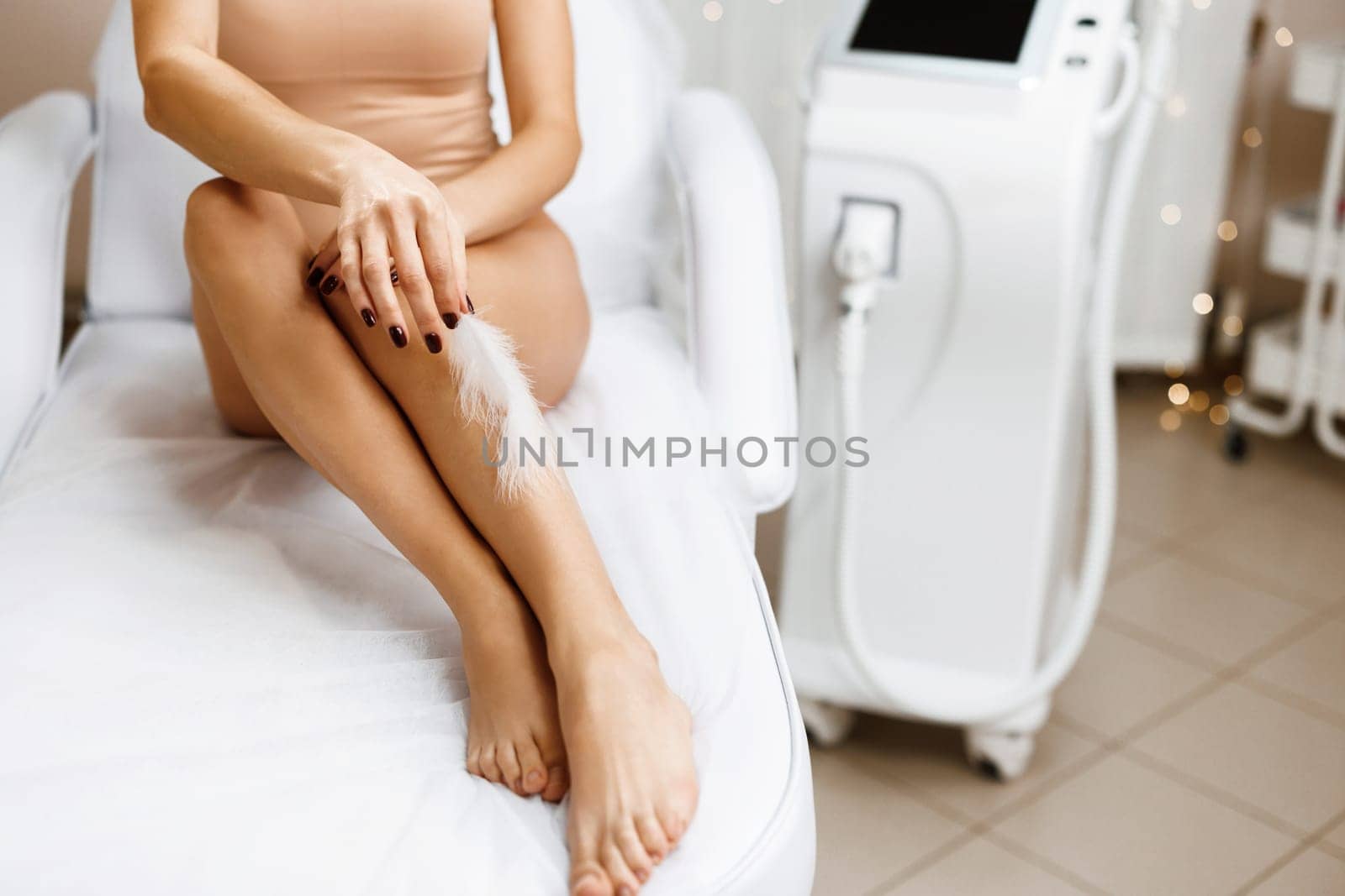 Female feet with smooth skin and soft ostrich feathe. Woman touches her legs with white feather. Concepts of skin care and hair removal treatment.